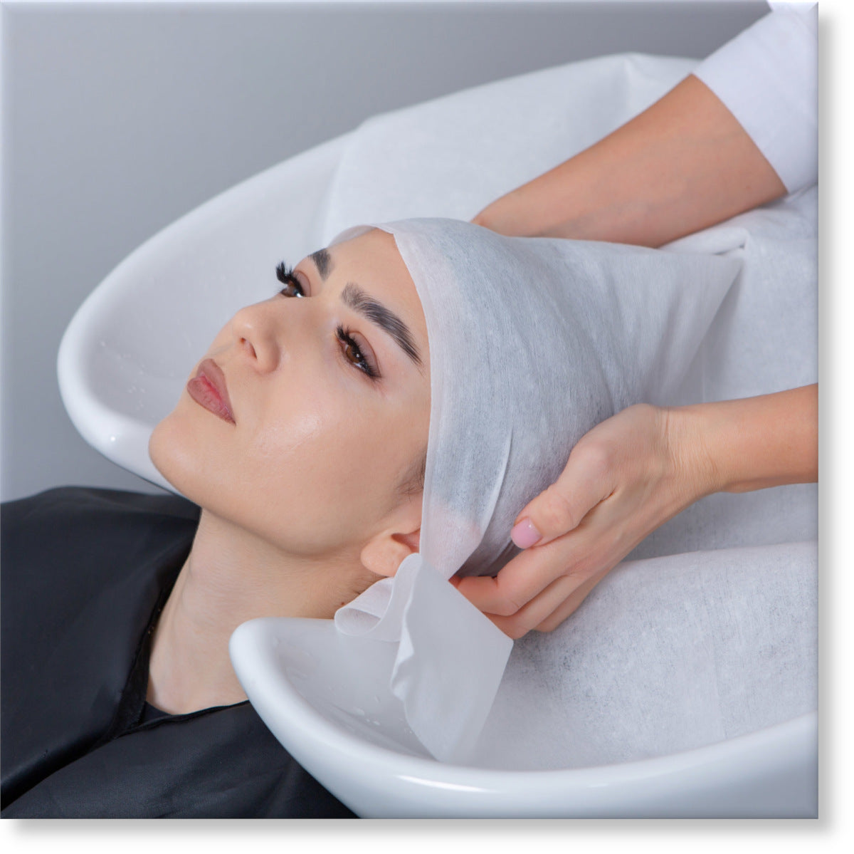  Image of a young woman reclining her head back about to have her hair wrapped in a disposable towel after washing her hair