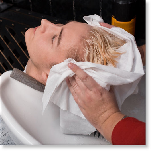 hands of a professional hairdresser wiping the clients hair with a white disposable towel after washing 