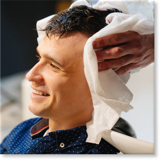 Image depicting a hairdresser wiping a clients hair with a disposable towel after washing hair in a barber shop. 