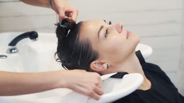 a short video clip depicting a young woman having her hair professionally washed and wrapped in a white disposable towel